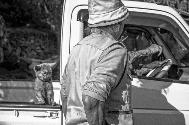Photograph of Man in front of a Truck with a Doggie in Back